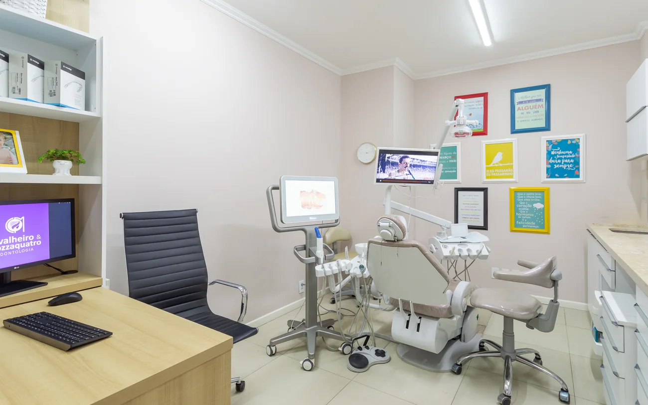 Consultório real com cadeira odontológica, equipamento, bancada clara e estante.